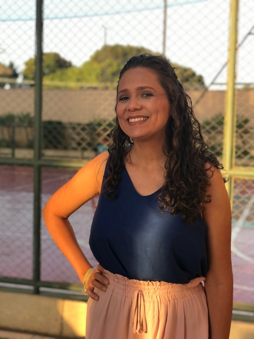 Lívia sorrindo, em pé, na quadra de uma escola